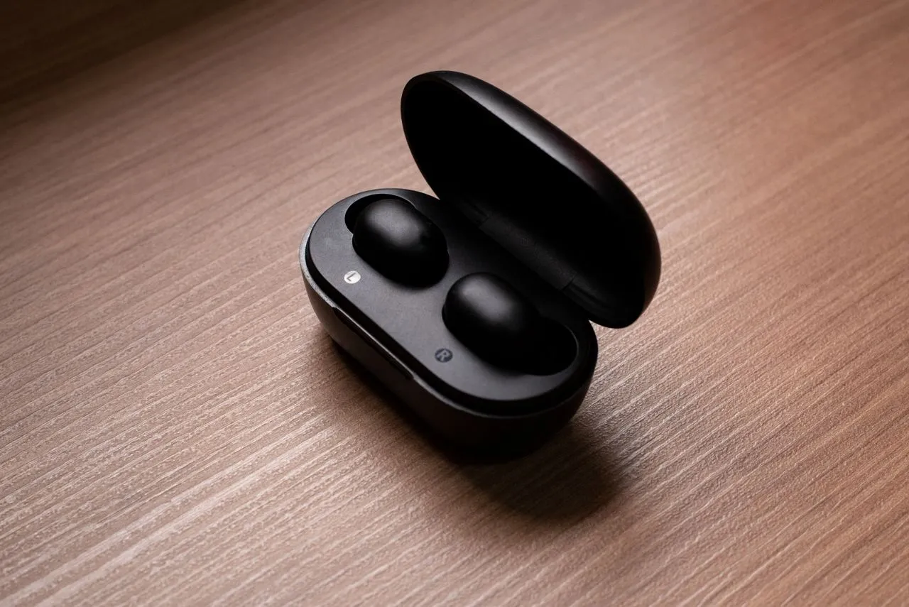Small black wireless earbuds sitting in an open charging case on a wooden table