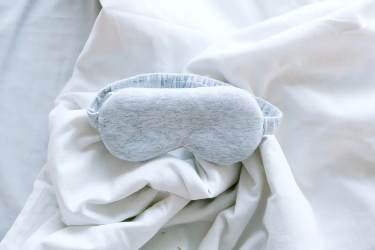 Soft gray jersey sleep mask resting on rumpled white bedding