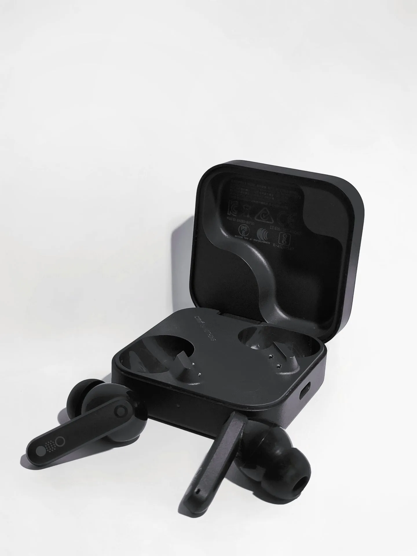 Black wireless earbuds lying beside an open charging case on a white backdrop