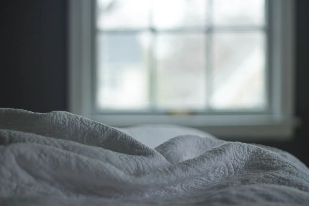 Soft white quilted bedding in the gray light of a bedroom window